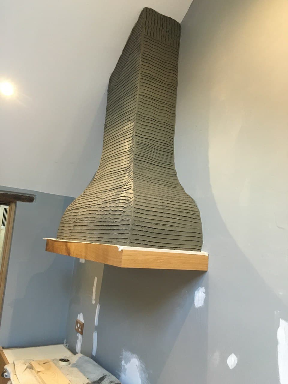Finished bespoke chimney hood with hand-scored textured render and oak mantel shelf by Spiby Build