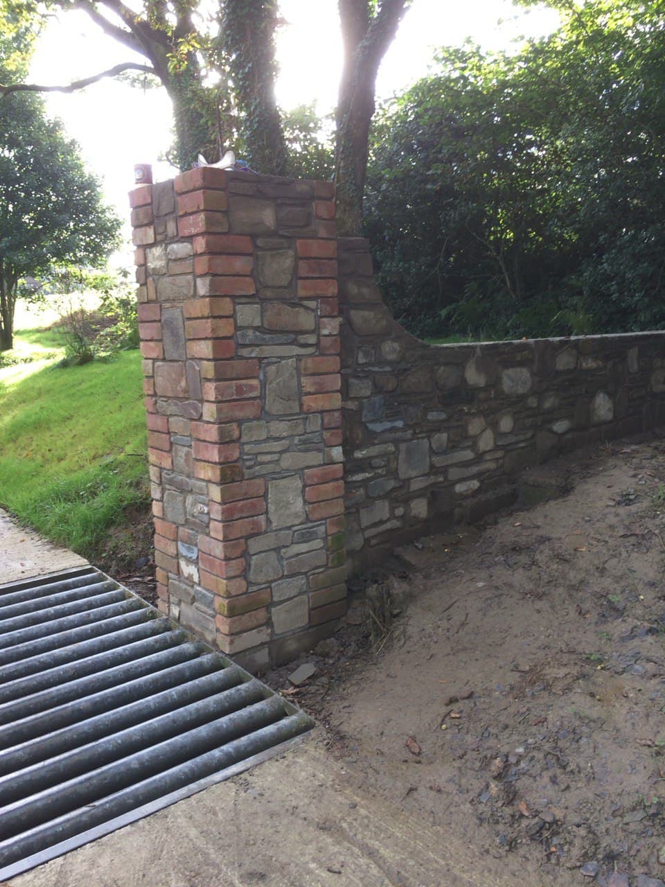 Detail of reclaimed brick and stone entrance pillar showing brick quoins and natural stone coursework with drainage grid