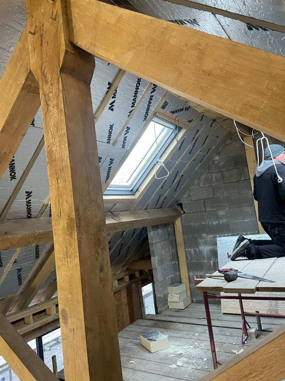 Interior view of oak timber roof frame with Mannok insulation boards fitted between rafters and a velux skylight at Thornbury Devon new build