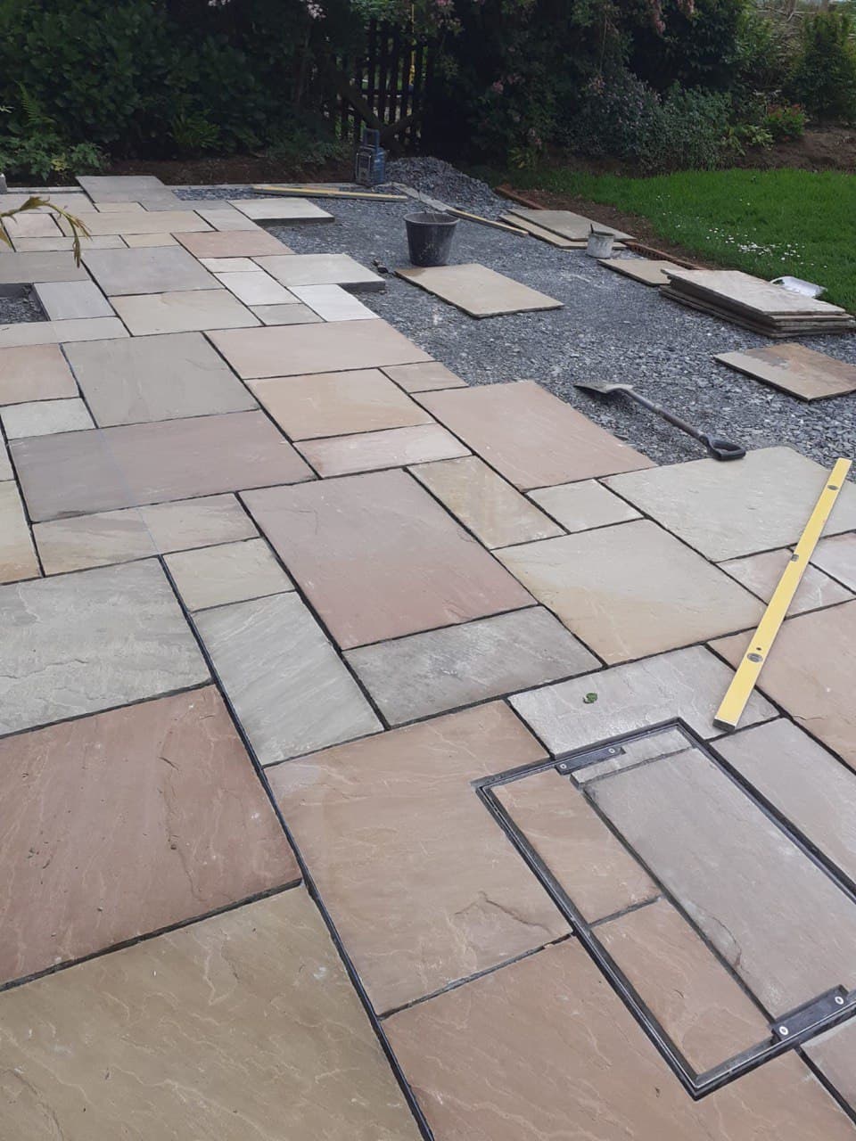 Indian sandstone patio being laid in a mixed pattern with spirit level and recessed inspection cover at a residential garden