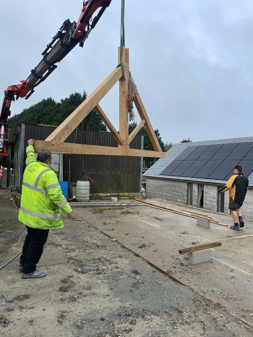 Spiby Build team members guiding an oak roof truss into position on a new build construction site