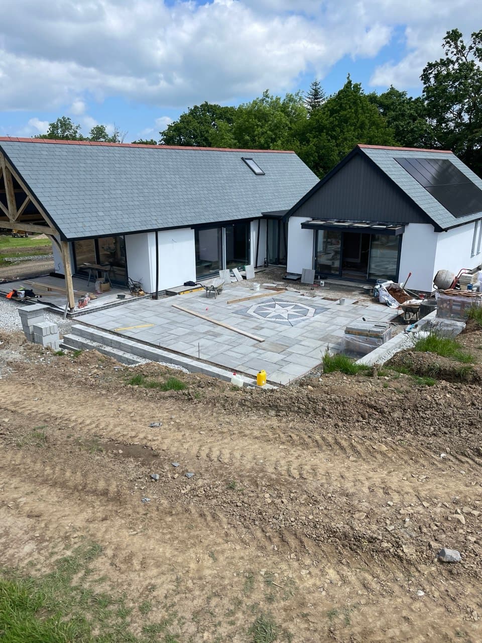 Completed front view of Thornbury Devon new build with white render slate roof oak carport and natural stone patio with compass rose