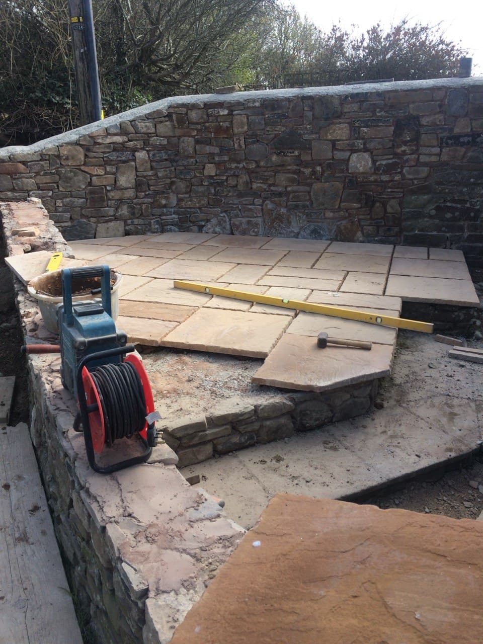 Natural sandstone patio being laid with spirit level on raised stone wall platform in North Cornwall