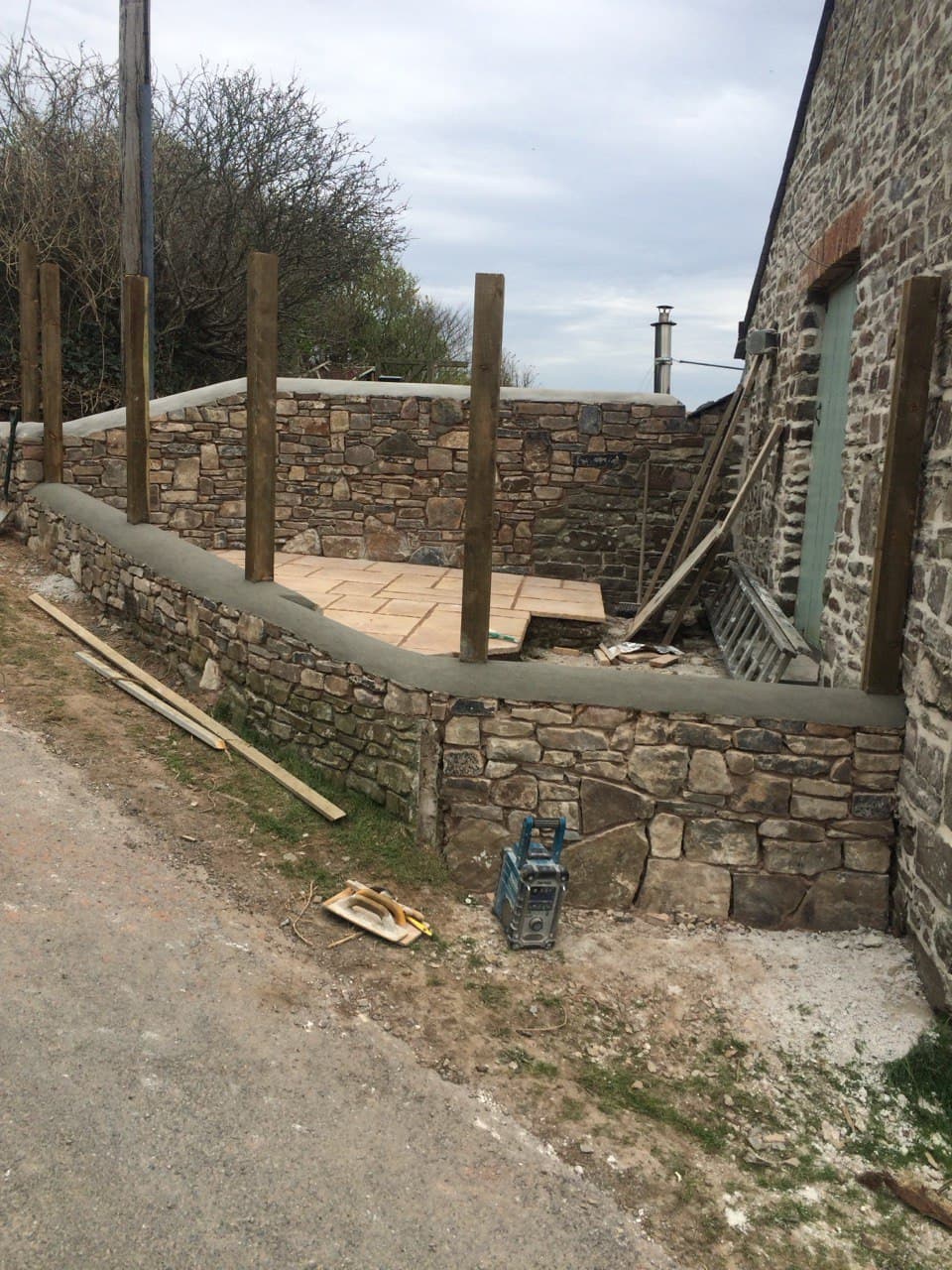 Completed raised patio with natural stone retaining walls and timber fence posts at a North Cornwall cottage